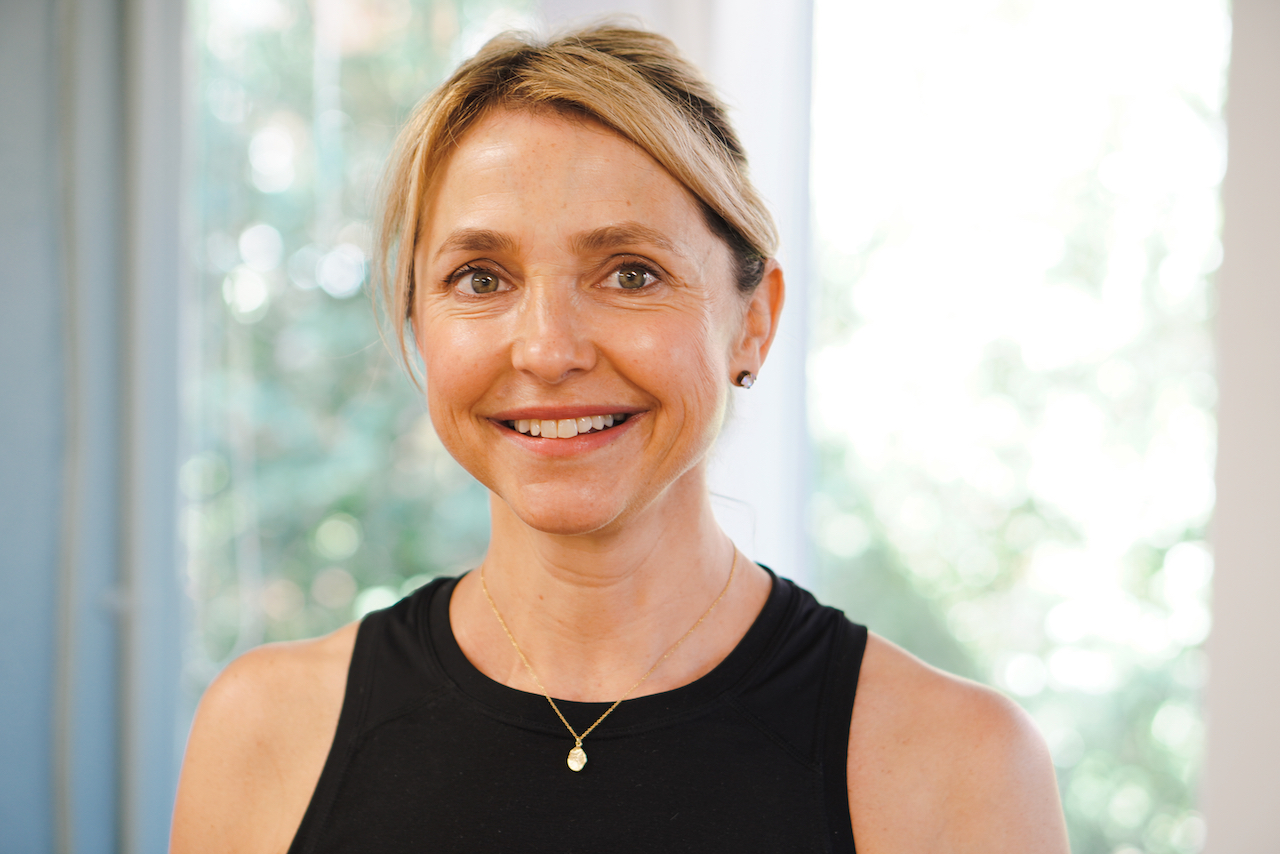Suzy Titford, smiling to camera, green foliage through a window behind her