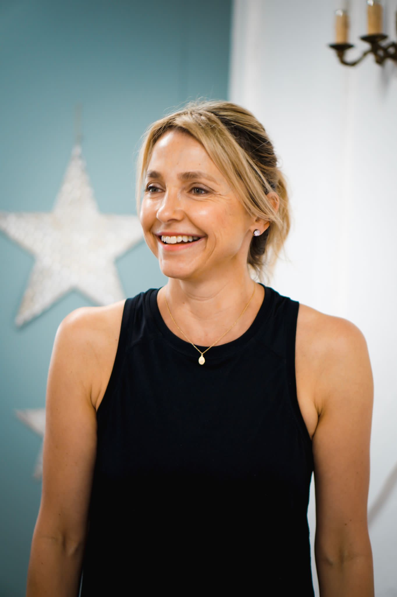 Suzy Titford smiling, in a black vest, in front of a teal wall with a large white star